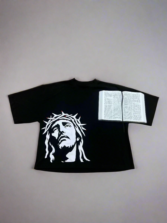 Black t-shirt with a white graphic of a bearded figure on a wooden floor with an open book.